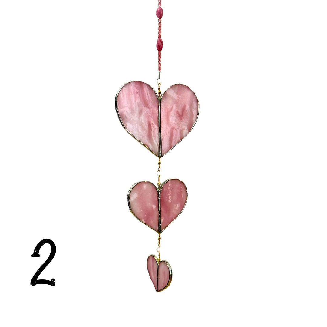 A stained glass suncatcher with three pink marbled glass heart panels with a pink beaded cord 
