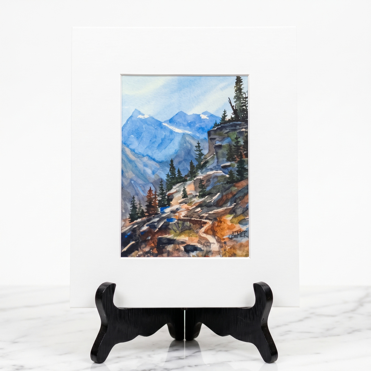 Discover high-altitude tranquility with Stark Mountain Studio's matted print of a Bobbe Almer watercolor hiking trail in Western Montana's rugged mountains.