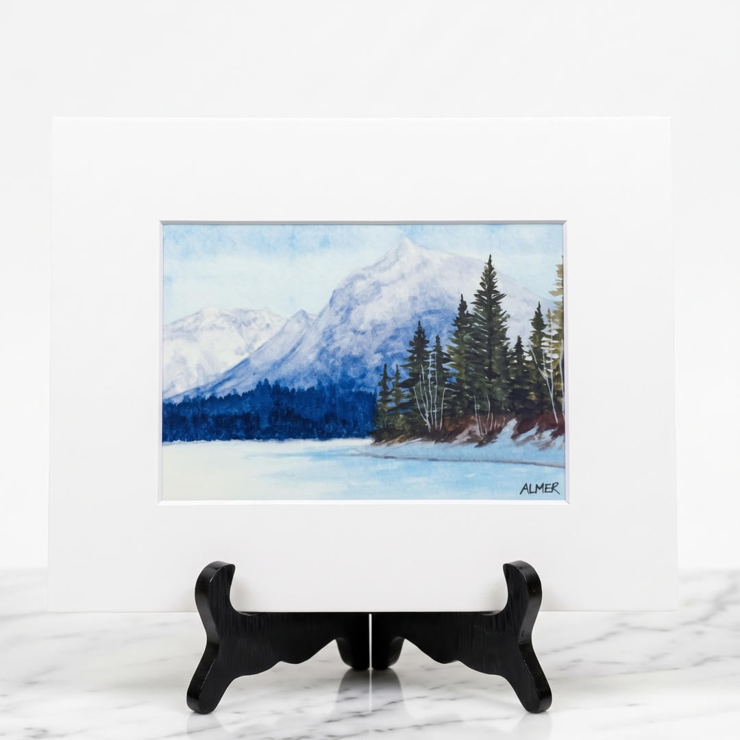 Bring Glacier National Park home with the Snowy Lake McDonald Matted Print by Stark Mountain Studio, featuring a watercolor painting by Bobbe Almer.
