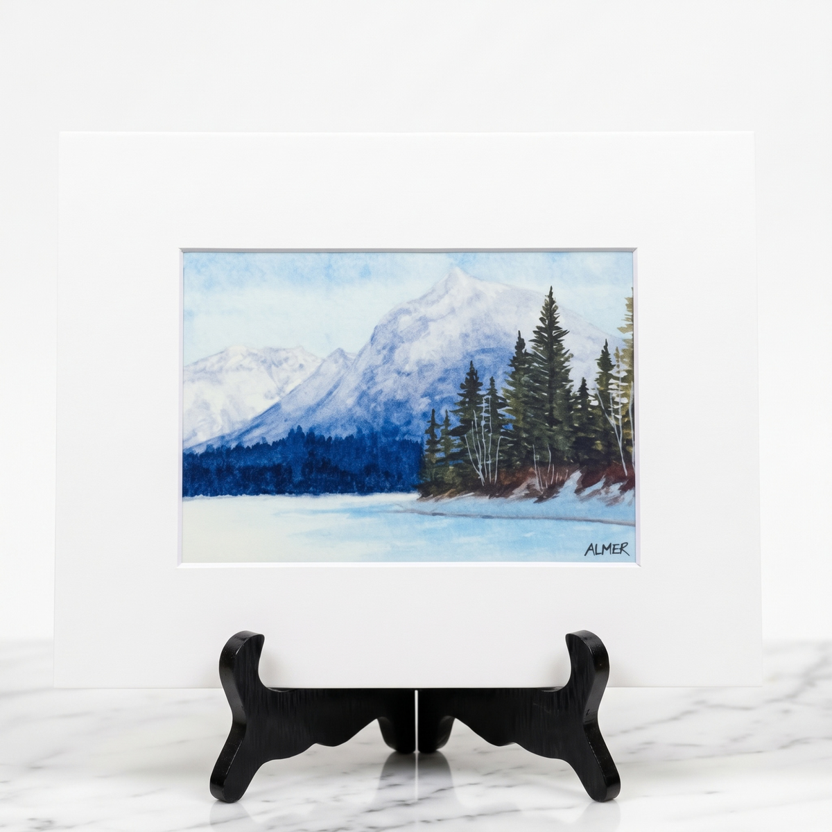 Bring Glacier National Park home with the Snowy Lake McDonald Matted Print by Stark Mountain Studio, featuring a watercolor painting by Bobbe Almer.