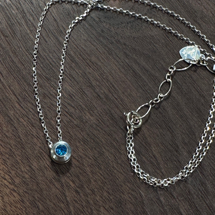 A cubic zirconia gemstone colored rich Sapphire Blue for a September Birthstone Necklace, set in sterling silver on a dark wood background