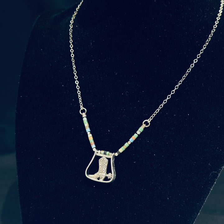 A sterling silver boot pendant and turquoise necklace on a black background.