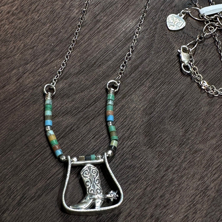 A sterling silver boot pendant and turquoise necklace on a dark wood background.