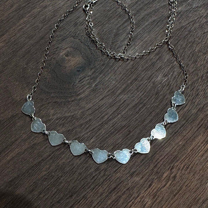 A strand of sterling silver hearts on a silver chain necklace on a dark wood background