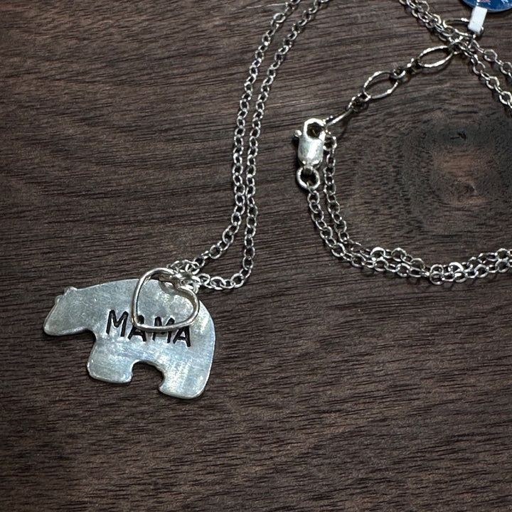 A silver necklace with a bear shaped pendant engraved with the word &