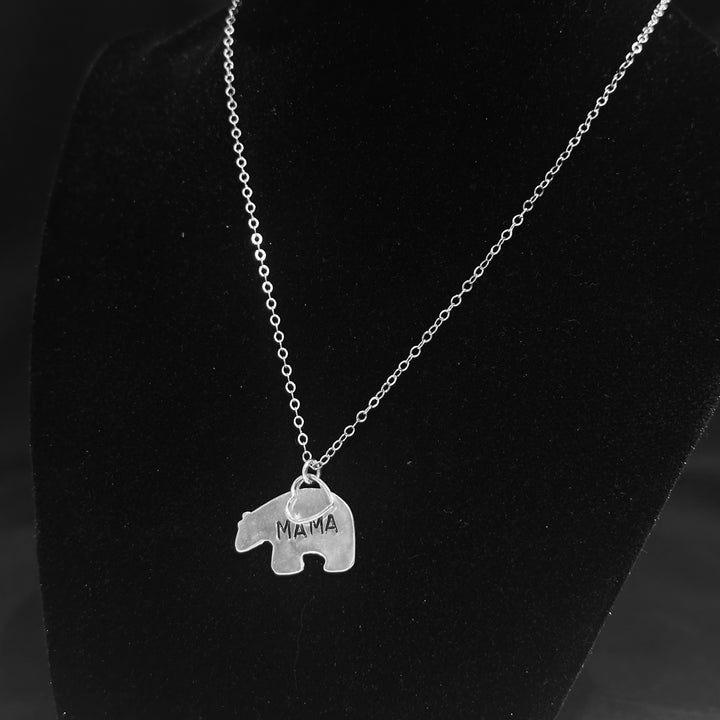 A silver necklace with a bear shaped pendant engraved with the word &