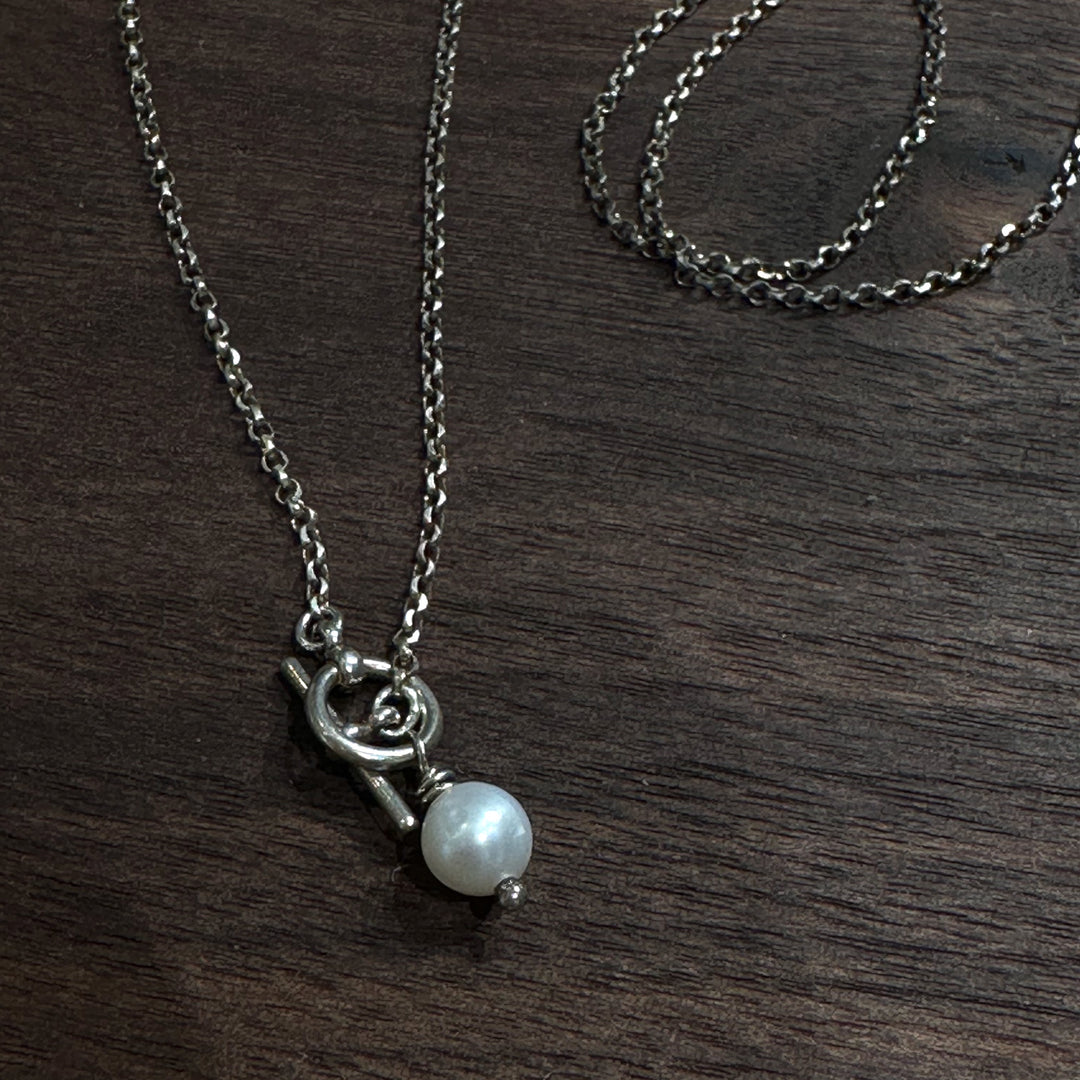 A sterling silver toggle clasp necklace with a pearl bead on a dark wood background