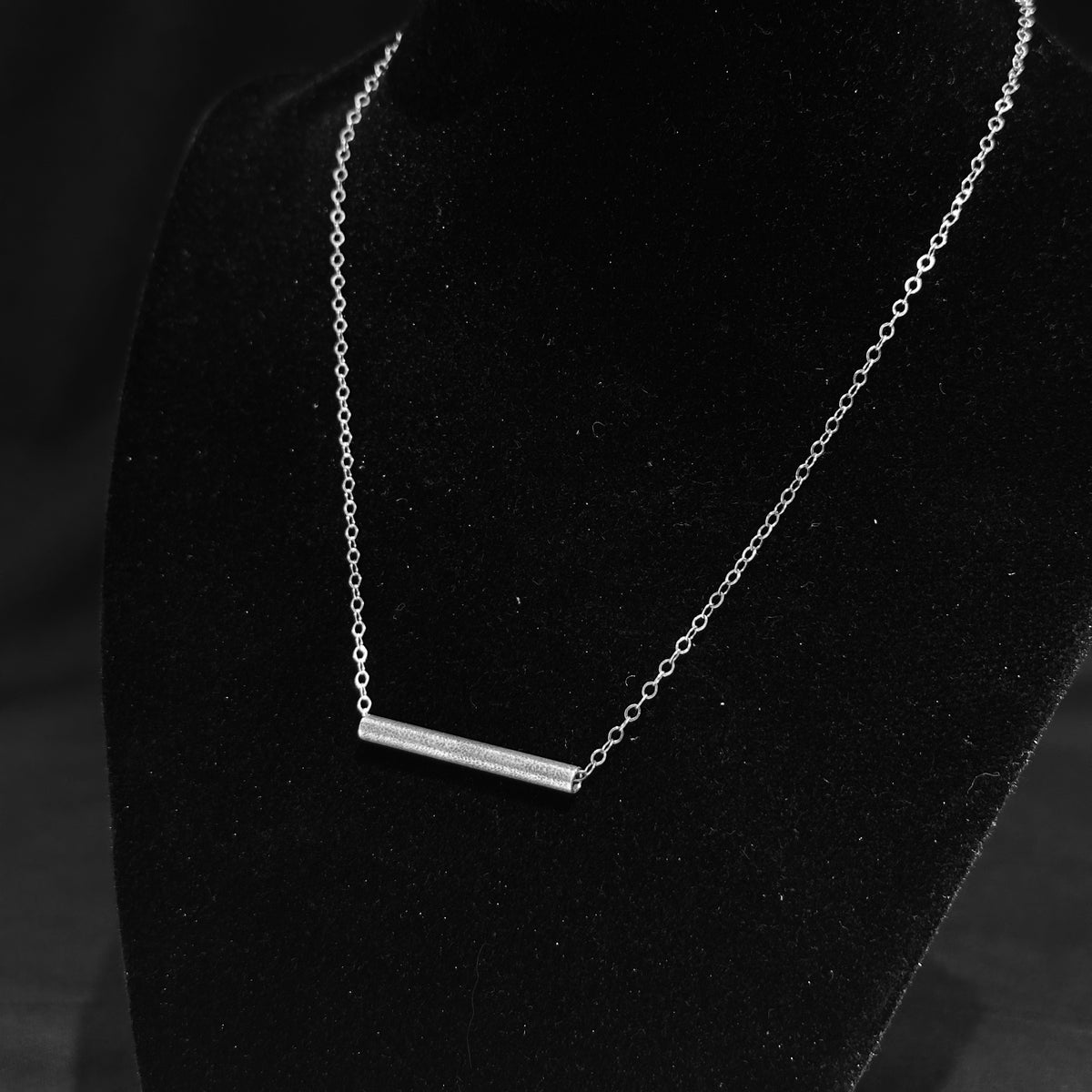 A sterling silver textured tube on a silver chain necklace on a black background