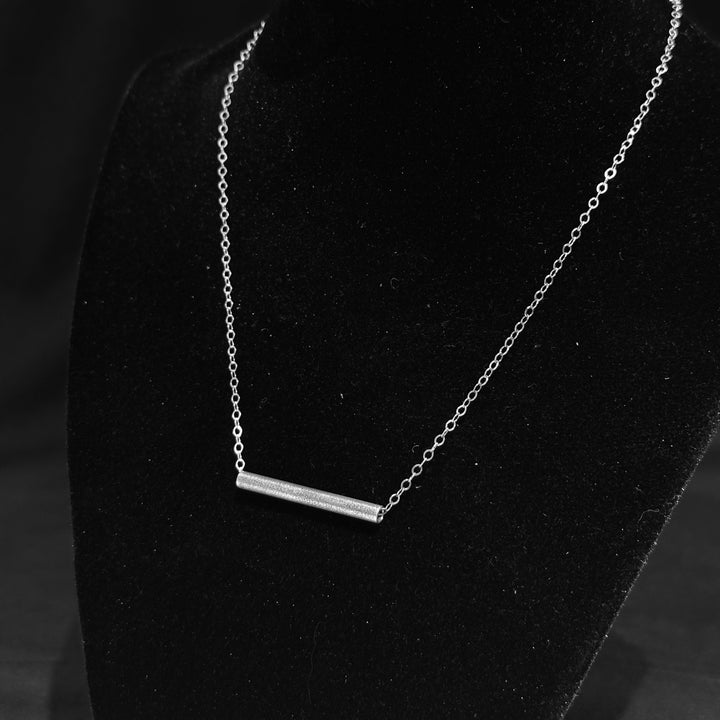 A sterling silver textured tube on a silver chain necklace on a black background