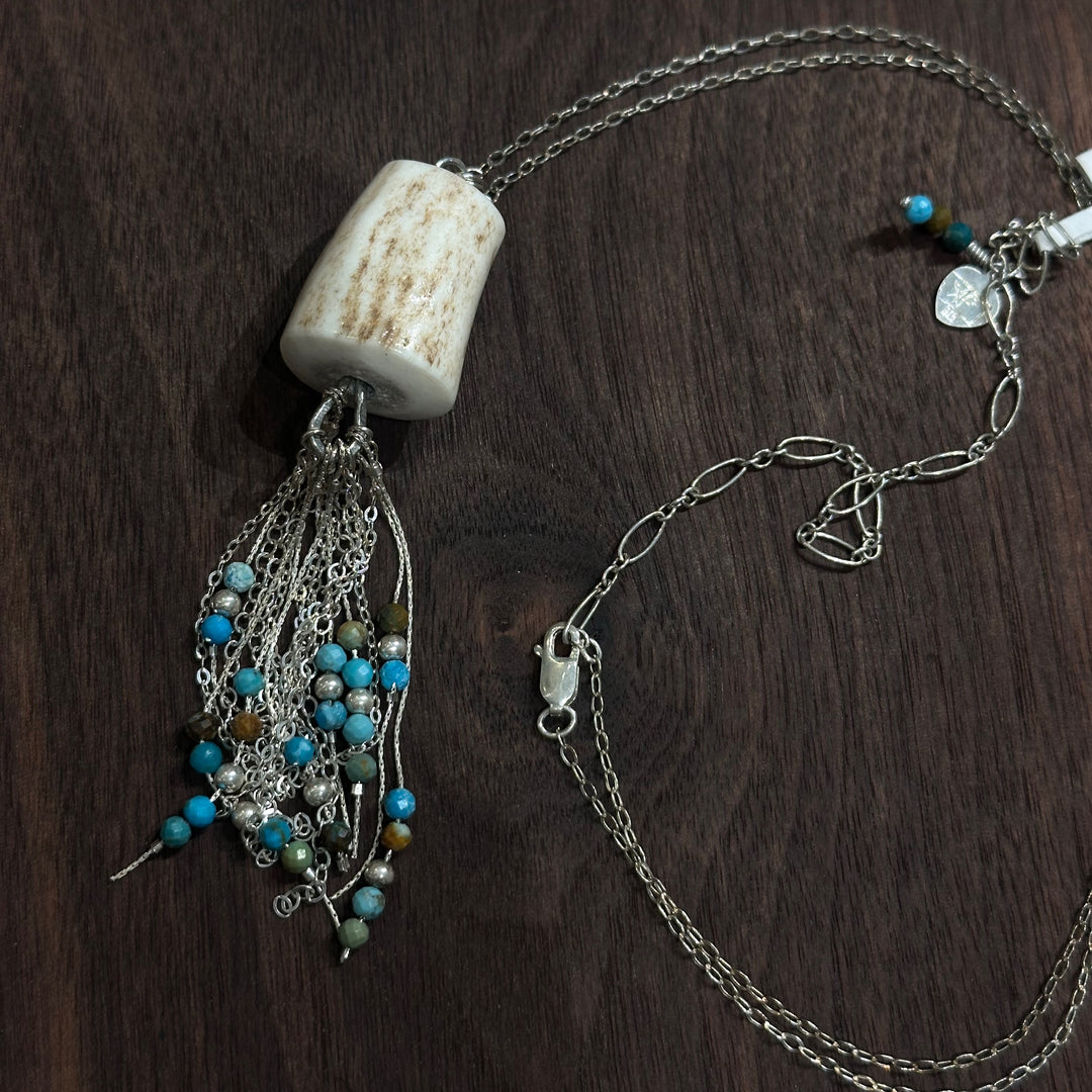 An antler pendant with silver chain and turquoise beads on a silver chain on a dark wood background