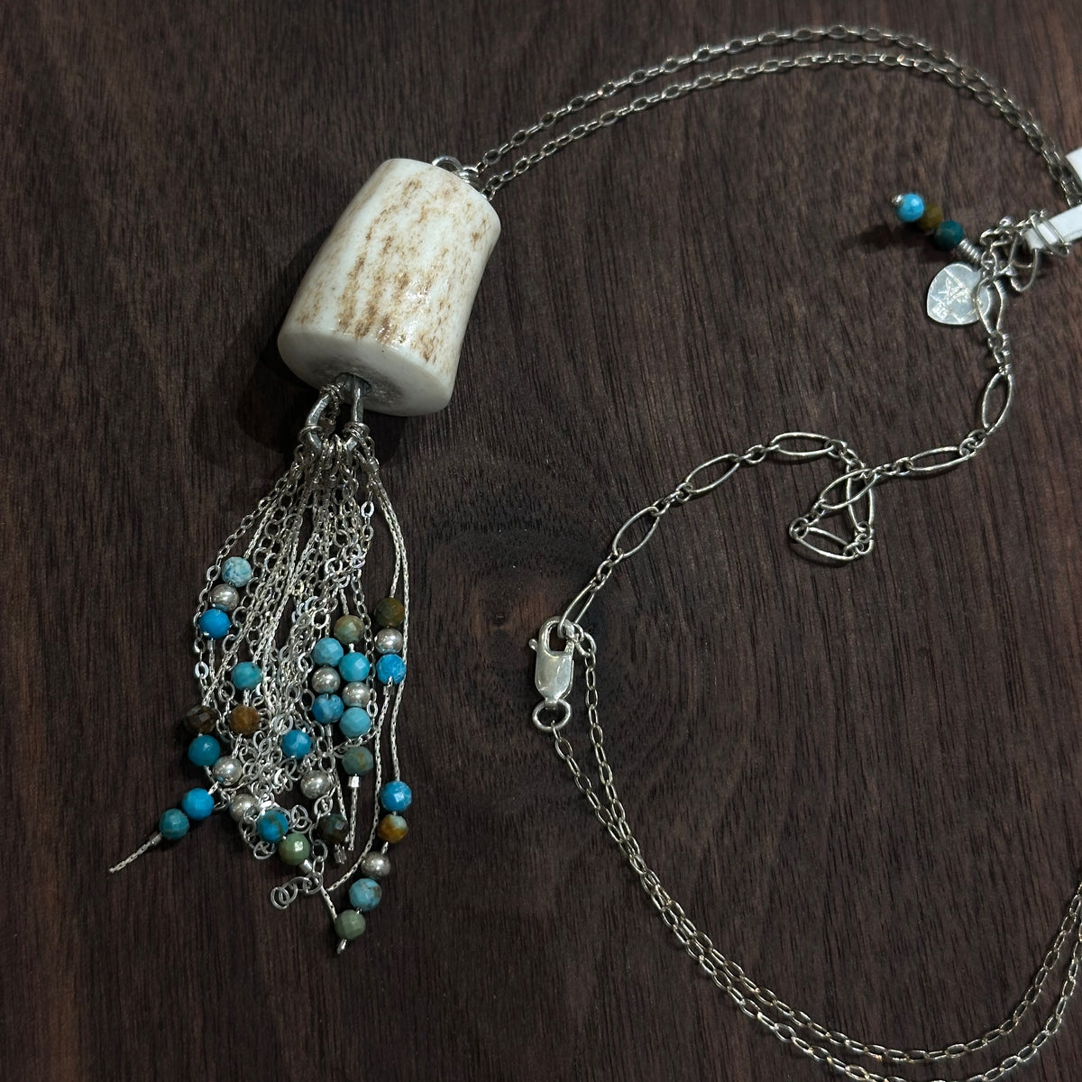 An antler pendant with silver chain and turquoise beads on a silver chain on a dark wood background