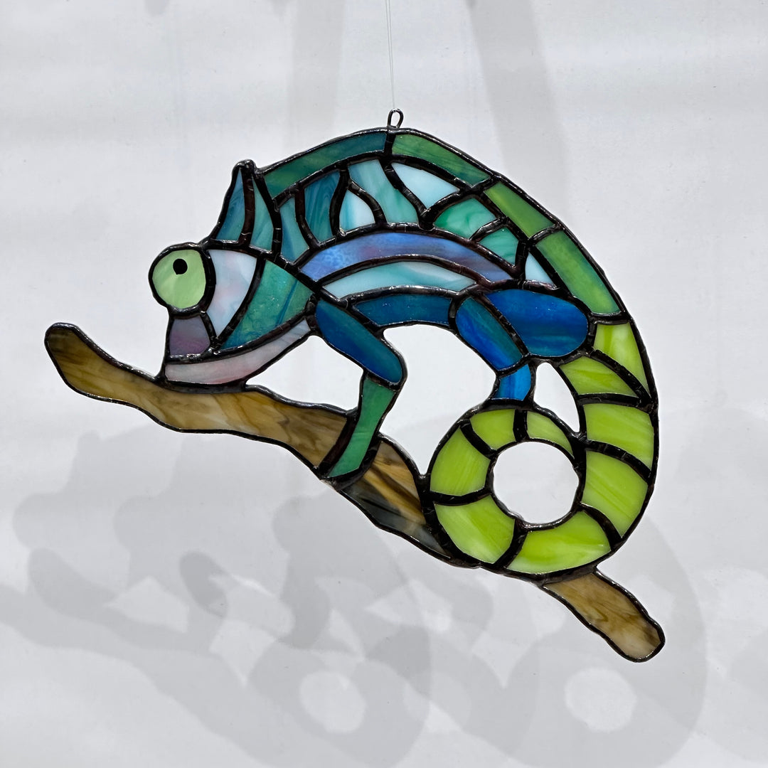 A stained glass chameleon on a stick in green, teal and blue glass