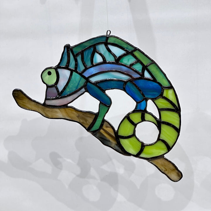 A stained glass chameleon on a stick in green, teal and blue glass