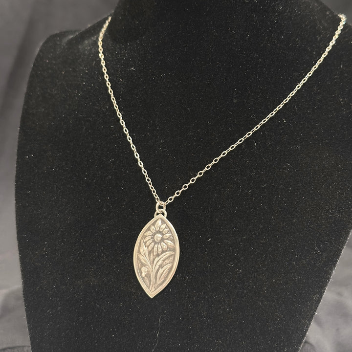 A sterling silver flower pendant necklace handmade by Cobblestone Designs of Montana on a black necklace form