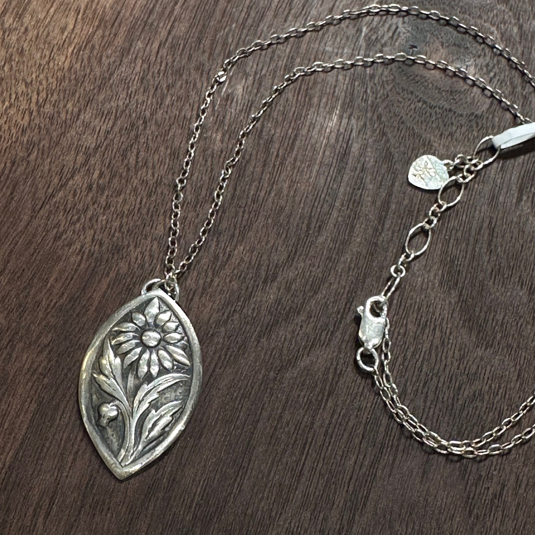 A sterling silver flower pendant necklace handmade by Cobblestone Designs of Montana on a dark wood background