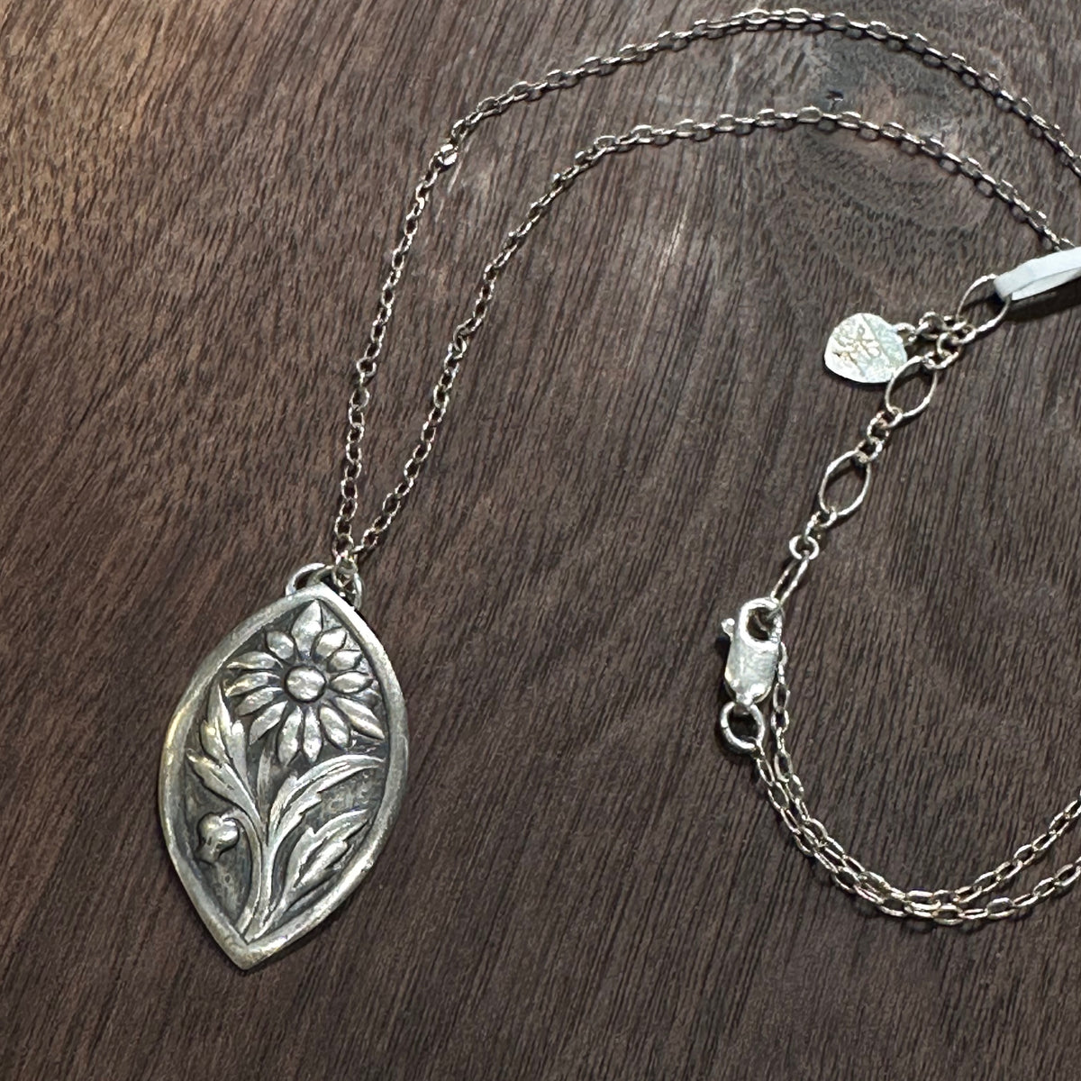 A sterling silver flower pendant necklace handmade by Cobblestone Designs of Montana on a dark wood background