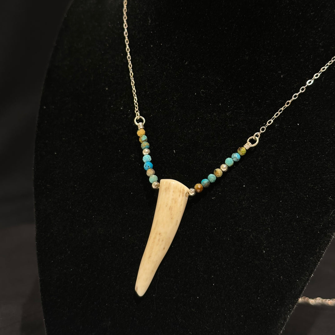An antler tip necklace with turquoise and silver beads on a silver chain. Displayed on a black background
