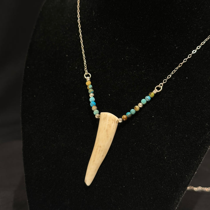 An antler tip necklace with turquoise and silver beads on a silver chain. Displayed on a black background