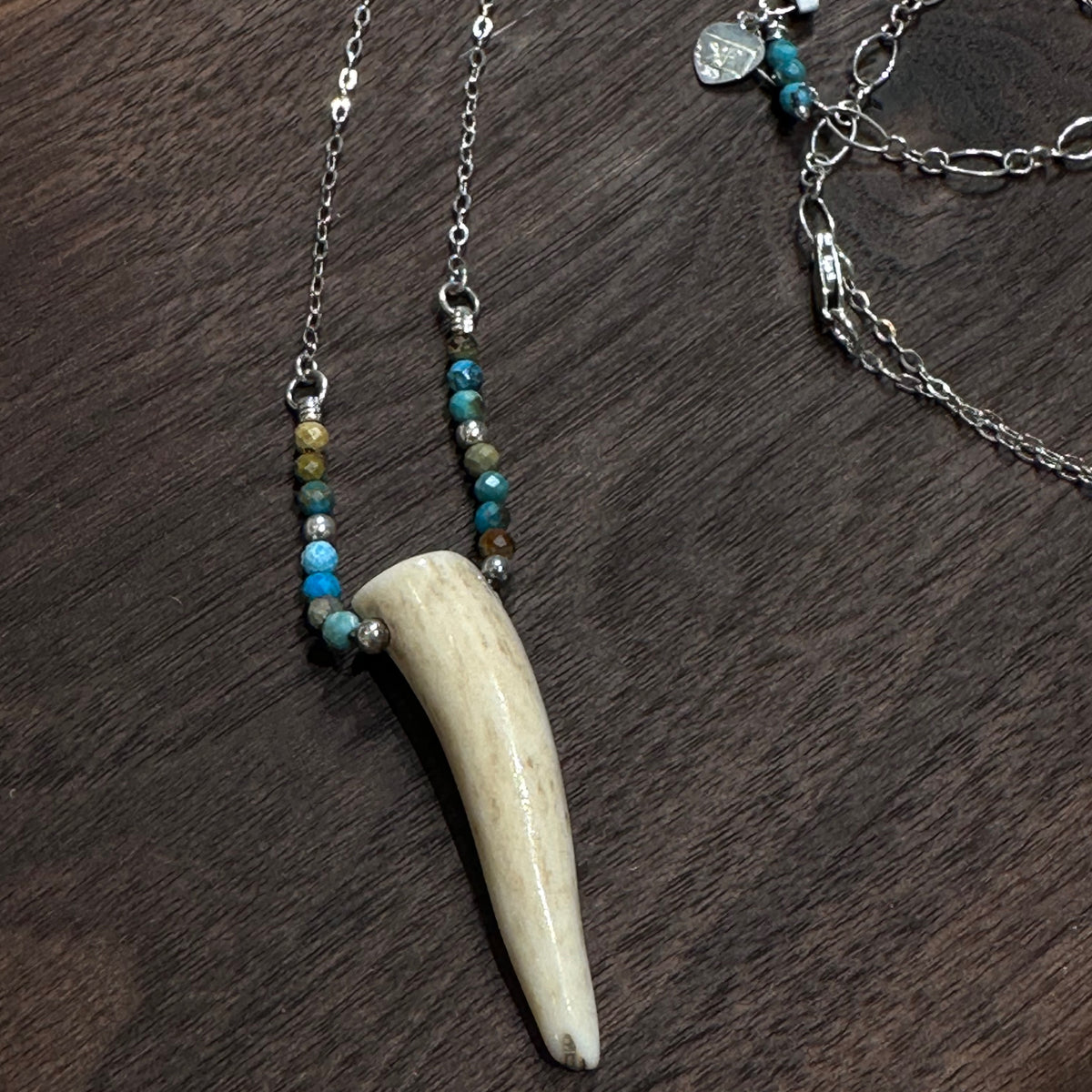 An antler tip necklace with turquoise and silver beads on a silver chain. Displayed on a dark wood background