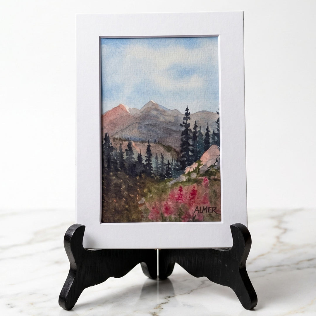 Bring home alpine beauty with the 5x7 Twin Peak Blooms matted watercolor print by Bobbe Almer. Features mountain peaks, pine forests, &amp; vibrant pink wildflowers.