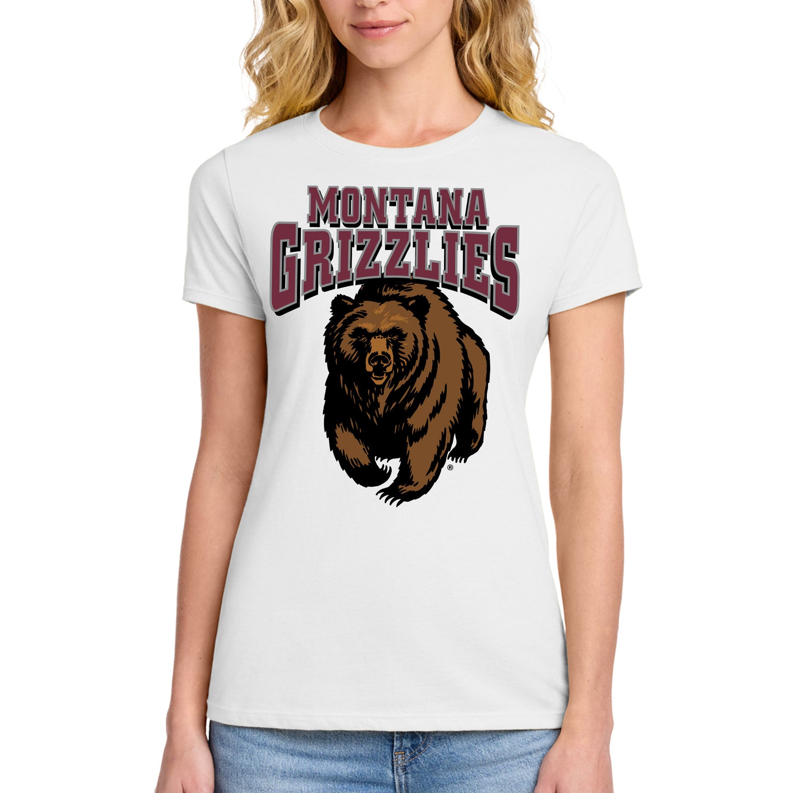 A woman wearing a white short-sleeve graphic T-shirt with 'MONTANA GRIZZLIES' text and a large charging grizzly bear illustration on the front, paired with blue jeans against a plain white background.