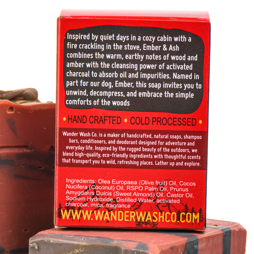 Display of three 5.25 oz bars of Ember &amp; Ash Bar Soap, Natural Cold Process Soap (wood, amber, sandalwood)—one in the box and two out of the box--made in Montana by Wander Wash Co, focused on back (ingredients list) against a white background