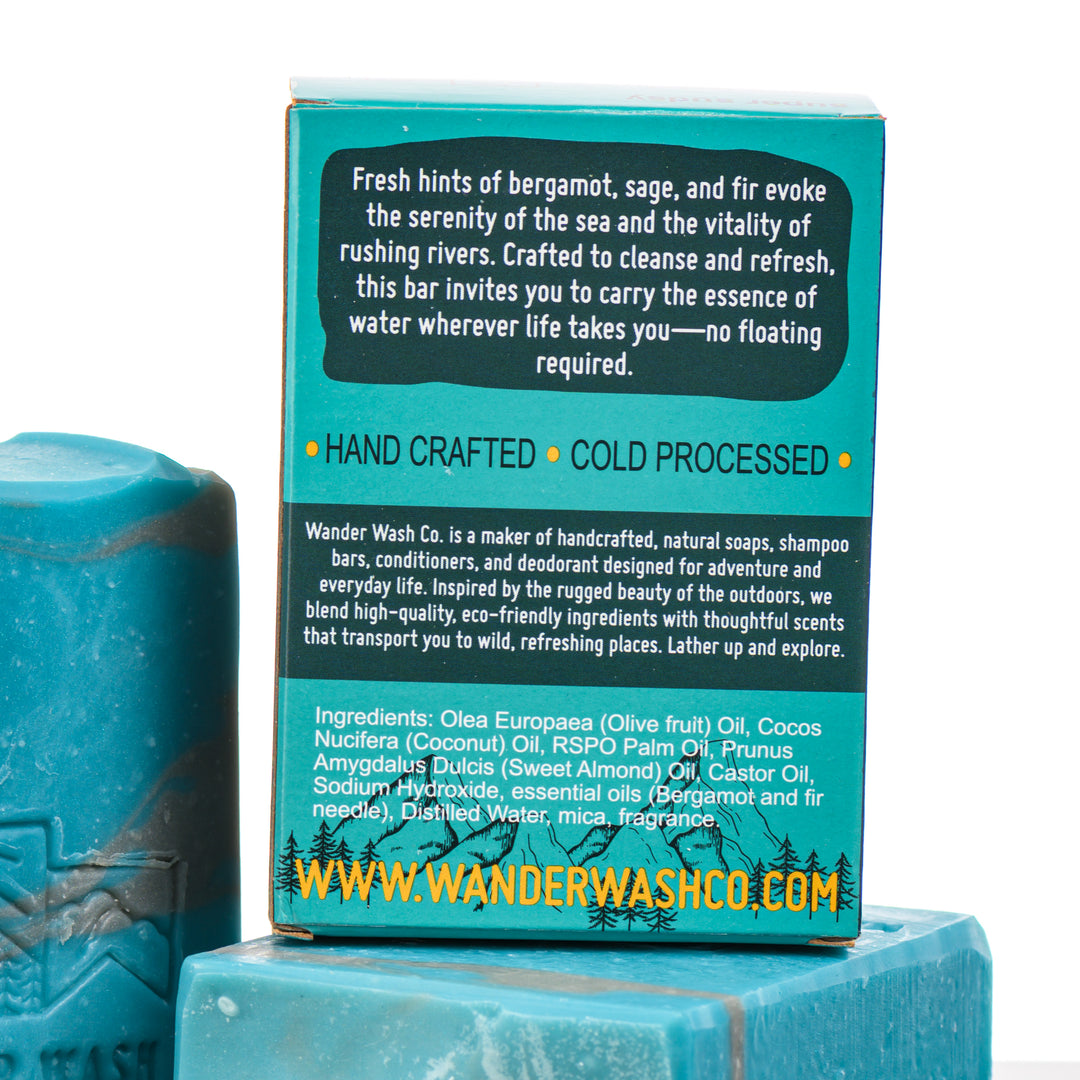 Display of three 5.25 oz bars of This Doesn’t Float, Natural Cold Process Soap (fresh water, bergamot)--one in the box and two out of the box--made in Montana by Wander Wash Co, focused on back (ingredients list) against a white background