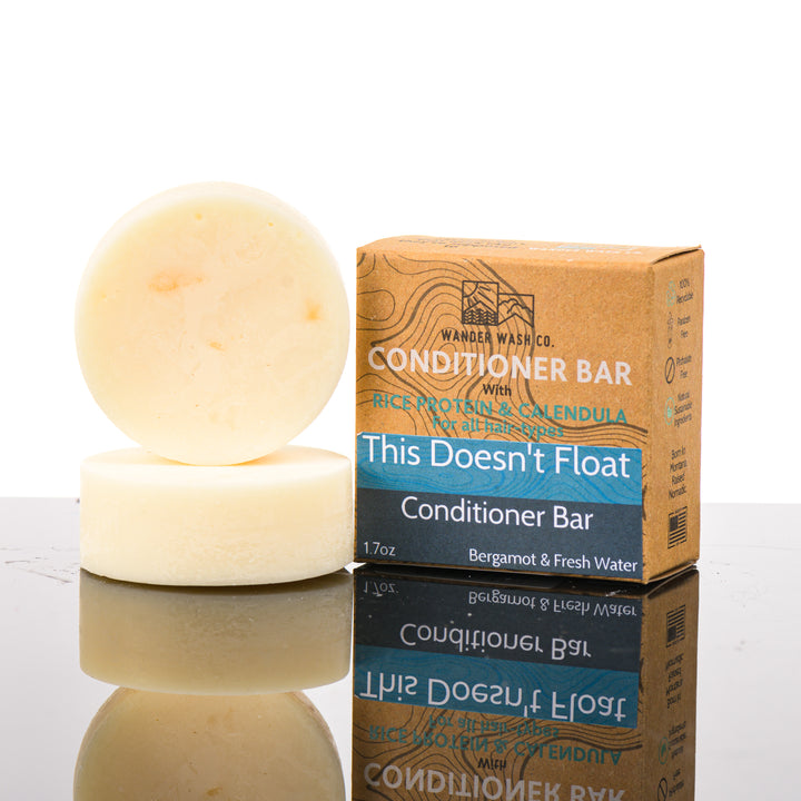 Display of three 1.7 oz bars of This Doesn’t Float Conditioner Bar (bergamot, fresh water)—one in the box and two out of the box--made in Montana by Wander Wash Co, against a white background