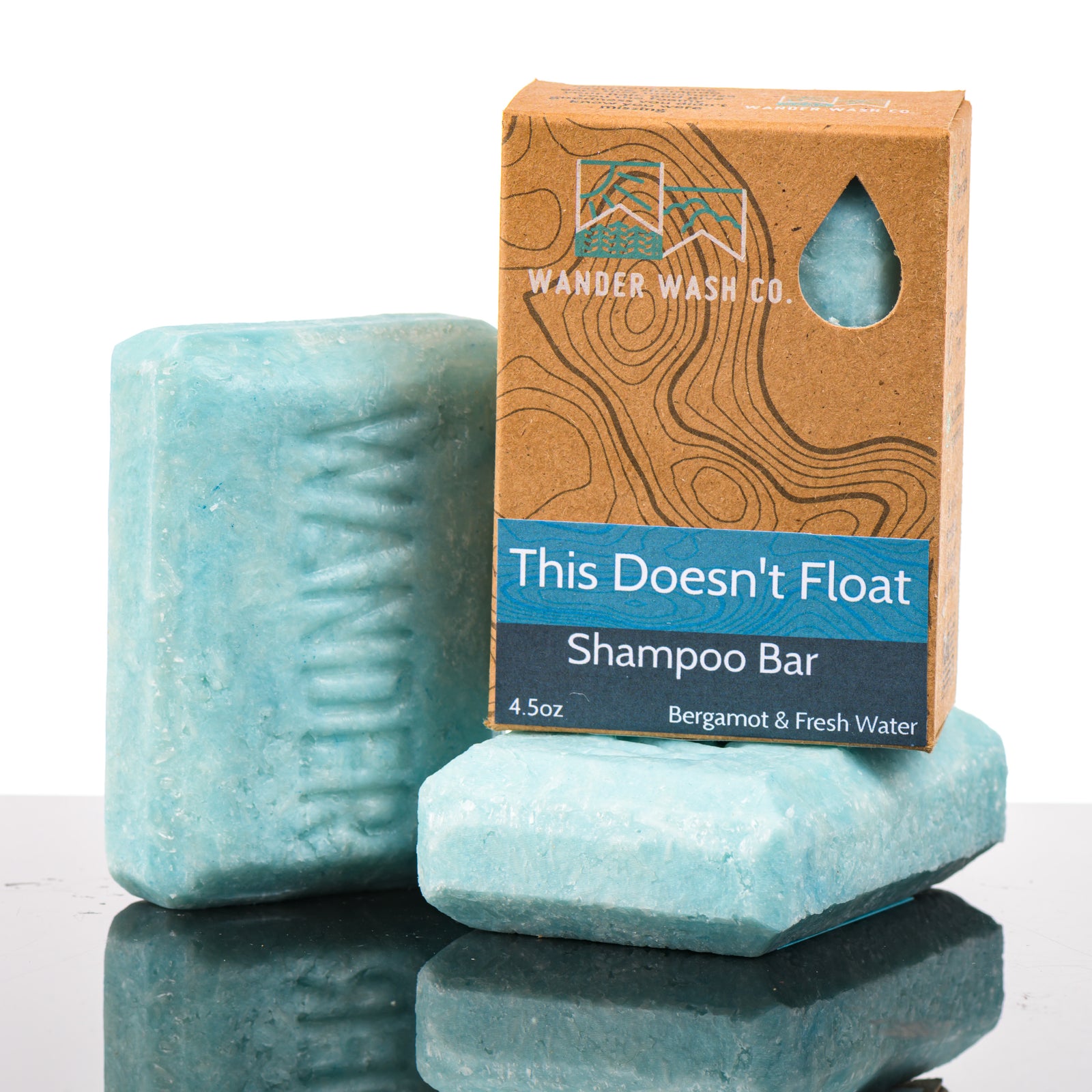 Display of three 4.5 oz bars of This Doesn’t Float Shampoo Bar (bergamot, fresh water)—one in the box and two out of the box--made in Montana by Wander Wash Co, against a white background