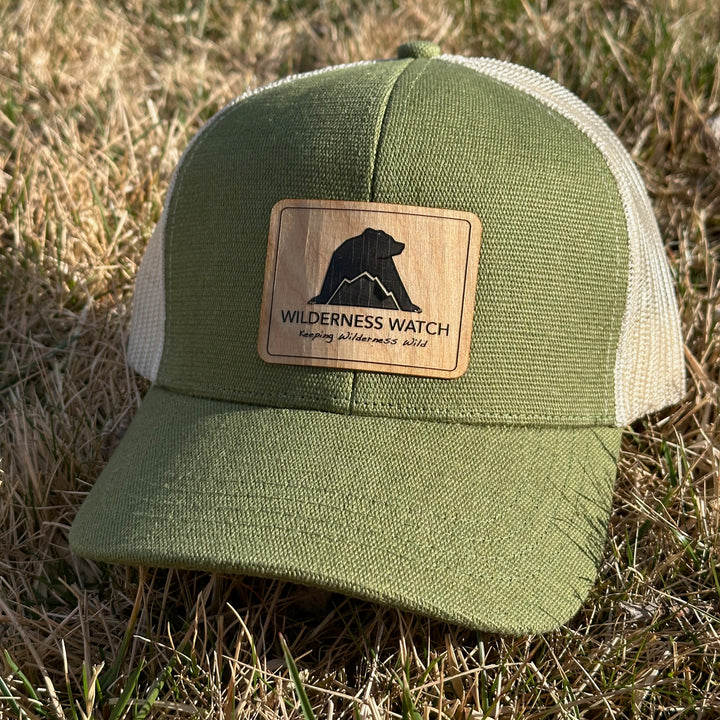 Green hemp trucker cap with a wood Wilderness Watch logo on grass