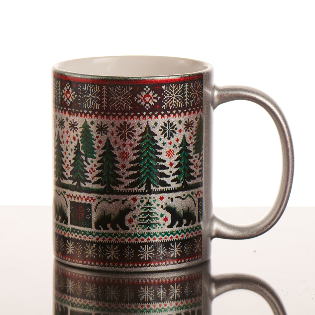 A silver mug with a bear, tree and snowflake pattern in the style of a knit sweater