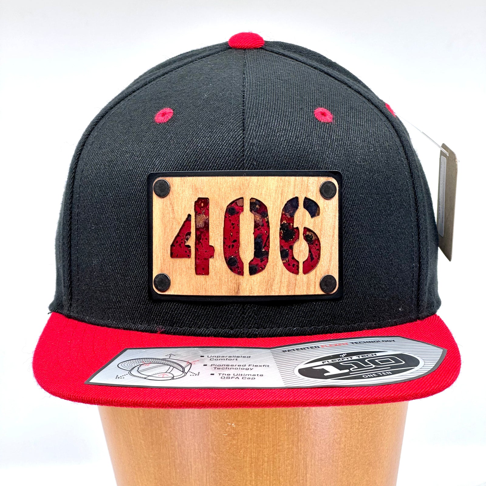 A flex fit, black and red flat bill hat with a wood and metal patch featuring 406, for the Montana area code, and red copper inlay.