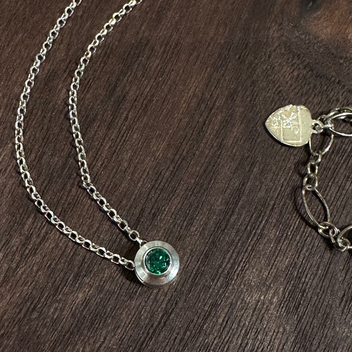 A cubic zirconia gemstone colored like a brilliant green Emerald for a May Birthstone Necklace, set in sterling silver on a dark wood background